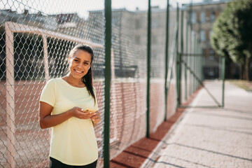 Smiling sporty woman standing near fence with smartphone