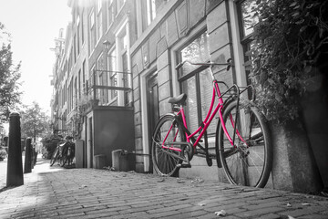 A picture of a lonely pink bike on the street by the channel in Amsterdam. The background is black and white.