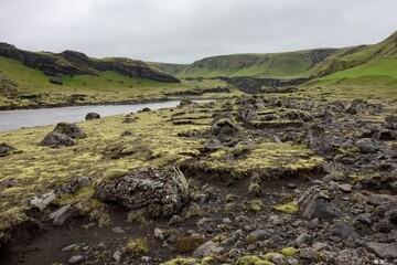 Landscape of Iceland in Kalfafell region with stones in grass, river and waterfall in background