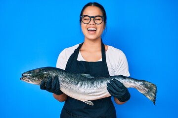 Young beautiful asian girl fishmonger selling fresh raw salmon smiling and laughing hard out loud...