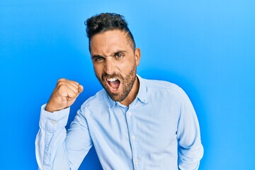 Handsome man with beard wearing casual clothes angry and mad raising fist frustrated and furious while shouting with anger. rage and aggressive concept.