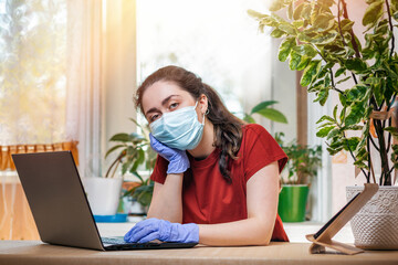 Quarantine.A young woman in a medical mask and gloves leaned lazily on her arm, looking bored. Home environment.The concept of freelancing, remote work and coronovirus