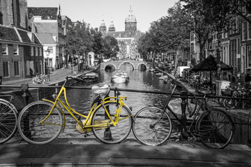 Fototapeta na wymiar A picture of a lonely yellow bike on the bridge over the channel in Amsterdam. The background is black and white.