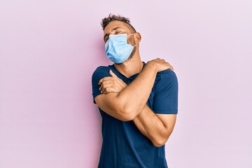 Handsome man with beard wearing medical mask hugging oneself happy and positive, smiling confident....