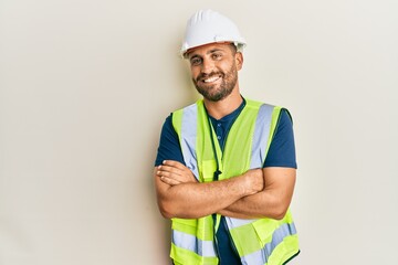 Handsome man with beard wearing safety helmet and reflective jacket happy face smiling with crossed...
