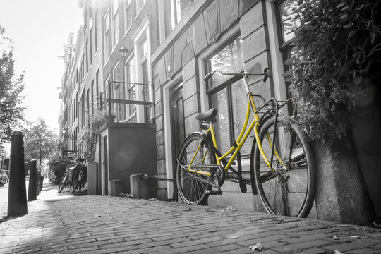A picture of a lonely yellow bike on the bridge over the channel in Amsterdam. The background is black and white. © shootingtheworld
