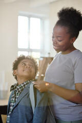 Happy young careful mother in casualwear helping her little son with backpack