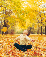a boy sitting in an autumn Park and having fun with maple trees