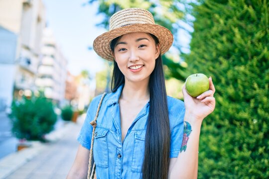Young chinese tourist woman eating green apple at the park.