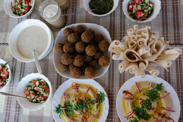 A table spread of middle-eastern dishes like hummus and falafel and salad