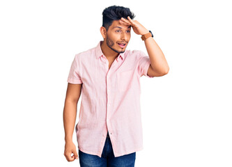 Handsome latin american young man wearing casual summer shirt very happy and smiling looking far away with hand over head. searching concept.