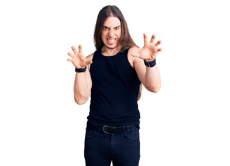 Young adult man with long hair wearing goth style with black clothes smiling funny doing claw gesture as cat, aggressive and sexy expression