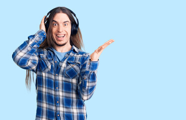 Young adult man with long hair listening to music using headphones celebrating victory with happy smile and winner expression with raised hands