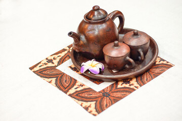 Traditional tea set or teh poci from Indonesia for serving Javanese black tea on a batik sheet. Consists of a pot, cups and a tray made of clay. Isolated, copy space.