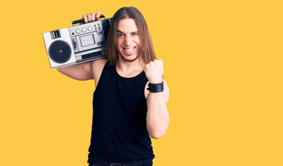 Young adult man with long hair wearing black clothes and holding boombox screaming proud, celebrating victory and success very excited with raised arms