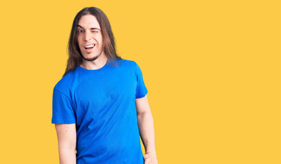 Young adult man with long hair wearing swimwear winking looking at the camera with sexy expression,...