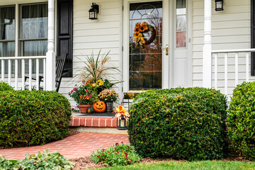 white colonial home with black shutters decorated for fall with jack-o-lantern and autumn foliage