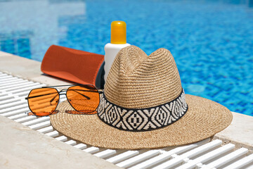 orange coloured beach accessories near swimming pool. Sun cream, sunglasses, music speaker and...