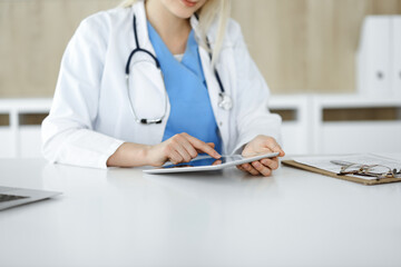 Unknown woman-doctor standing in clinic and using tablet pc, close-up. Data and best service in medicine and healthcare