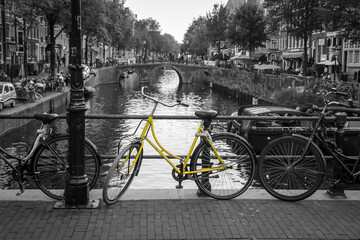 A picture of a lonely yellow bike on the bridge over the channel in Amsterdam. The background is black and white.