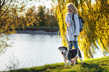 Naklejka na ściany i meble Woman standing in autumn park with her dog. Friendship between people and animal