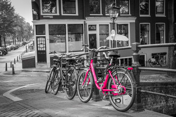 A picture of a pink bike on the bridge over the channel in Amsterdam. The background is black and white.