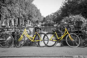 A picture of a two yellow bikes on the bridge over the channel in Amsterdam. The background is black and white.