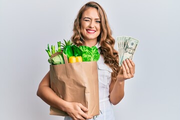 Young blonde girl holding paper bag with groceries winking looking at the camera with sexy...