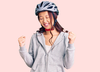 Young beautiful chinese girl wearing bike helmet very happy and excited doing winner gesture with arms raised, smiling and screaming for success. celebration concept.