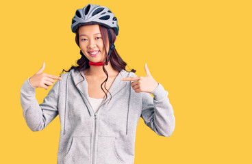 Young beautiful chinese girl wearing bike helmet looking confident with smile on face, pointing oneself with fingers proud and happy.