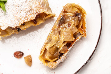 Traditional pieces of apple strudel with cinnamon, raisin, powdered sugar on light background. view...