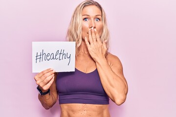 Middle age caucasian blonde woman wearing sportswear holding healthy banner covering mouth with...