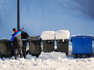 Worker throws trash into trash can on winter snowy day