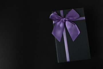only black black gift gift box with purple lilac fuchsia ribbon and bow on a black background with space for text copy space father's day new year Christmas birthday for men