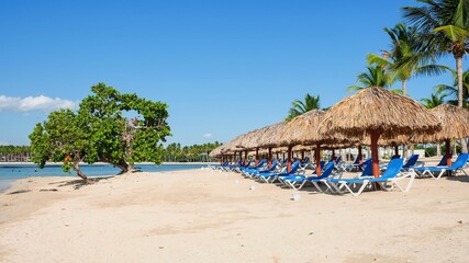 Row of empty lounger chairs under beach sun umbrellas made from palm tree leaves on the atlantic ocean coastline.