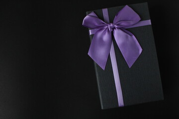 only black black gift gift box with purple lilac fuchsia ribbon and bow on a black background with space for text copy space father's day new year Christmas birthday for men