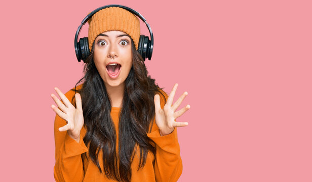 Beautiful brunette young woman listening to music using headphones celebrating crazy and amazed for success with arms raised and open eyes screaming excited. winner concept