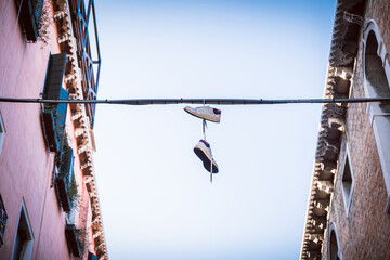 A pair of sneakers hanging on rope between houses - Shoes dangling on a power line in between typical houses