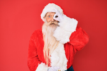 Old senior man with grey hair and long beard wearing traditional santa claus costume doing ok gesture with hand smiling, eye looking through fingers with happy face.