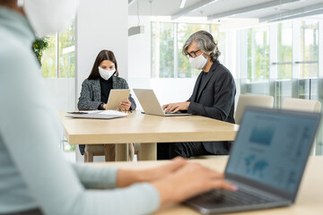 Two busy colleagues in smart casualwear and protective masks networking by table