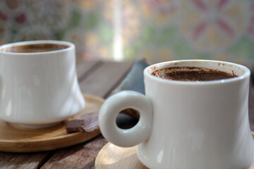 Turkish coffee with foam on top , made of fresh roasted and fine ground coffee beans, served in small ceramic cups on bamboo plates with Turkish delight or bitter chocolate pieces after breakfast
