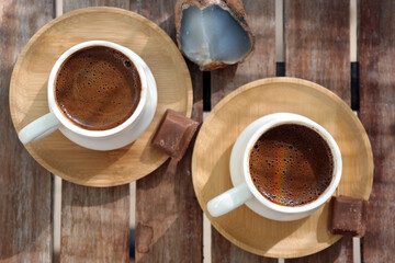 Turkish coffee with foam on top , made of fresh roasted and fine ground coffee beans, served in small ceramic cups on bamboo plates with Turkish delight or bitter chocolate pieces after breakfast