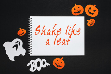 Happy halloween holiday concept. Notepad with text Shake like a leaf on black background with bats, pumpkins and ghosts