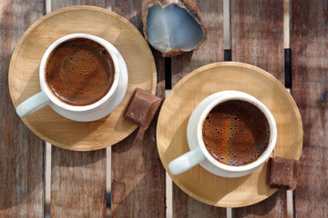 Turkish coffee with foam on top , made of fresh roasted and fine ground coffee beans, served in small ceramic cups on bamboo plates with Turkish delight or bitter chocolate pieces after breakfast