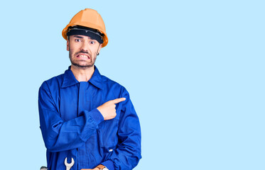 Young hispanic man wearing worker uniform pointing aside worried and nervous with forefinger, concerned and surprised expression