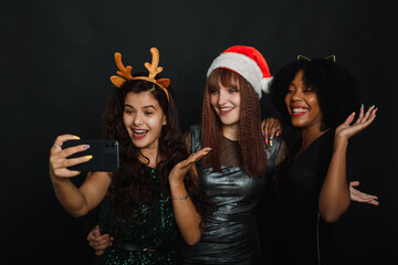 Group of friends at club making selfie and having fun. Cute young women posing with kissing face expression. Relaxed young women making selfie with friend on dark background during christmas