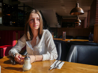 Pensive lonely woman is sitting at the table in a restaurant and looking to the window