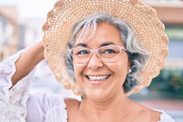 Middle age woman with grey hair smiling happy wearing summer hat outdoors