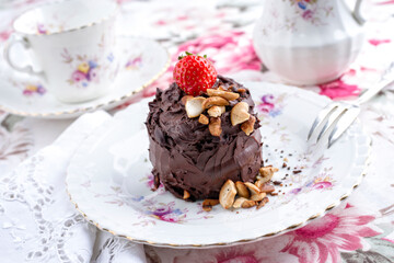 Traditional chocolate torte with cashew nuts and strawberry offered as close-up on a design bone China plate