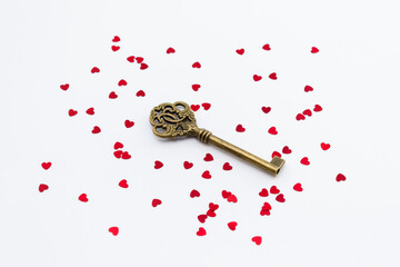 Metal old key decorated with red hearts confetti. The concept of the secret of love relationships. Selective focus